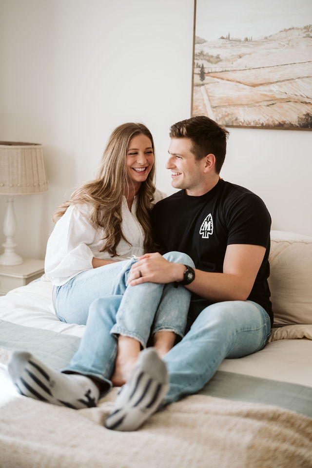 Couple smiling together on a bed during the Genesis Midwifery photography session.