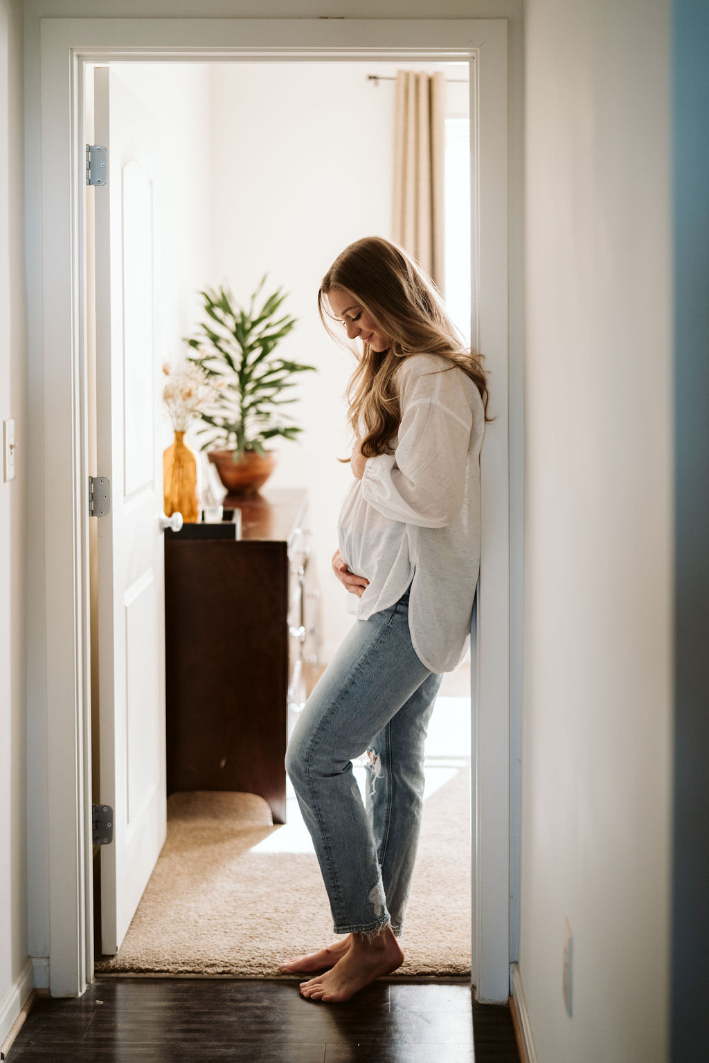 Expectant mother standing in a sunlit doorway.