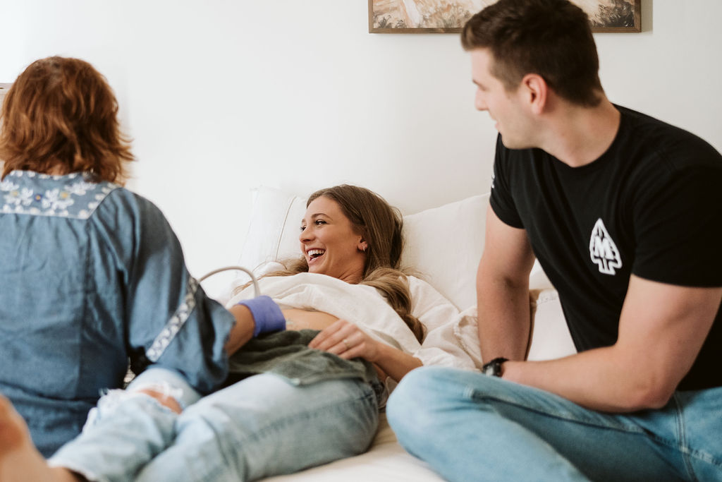 Midwife with a smiling couple during an in-home ultrasound appointment.