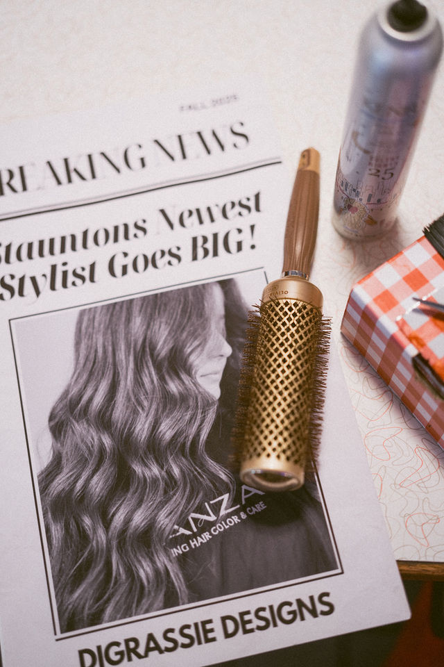 Hairbrush and styling products arranged with a DiGrassie Designs newspaper prop.
