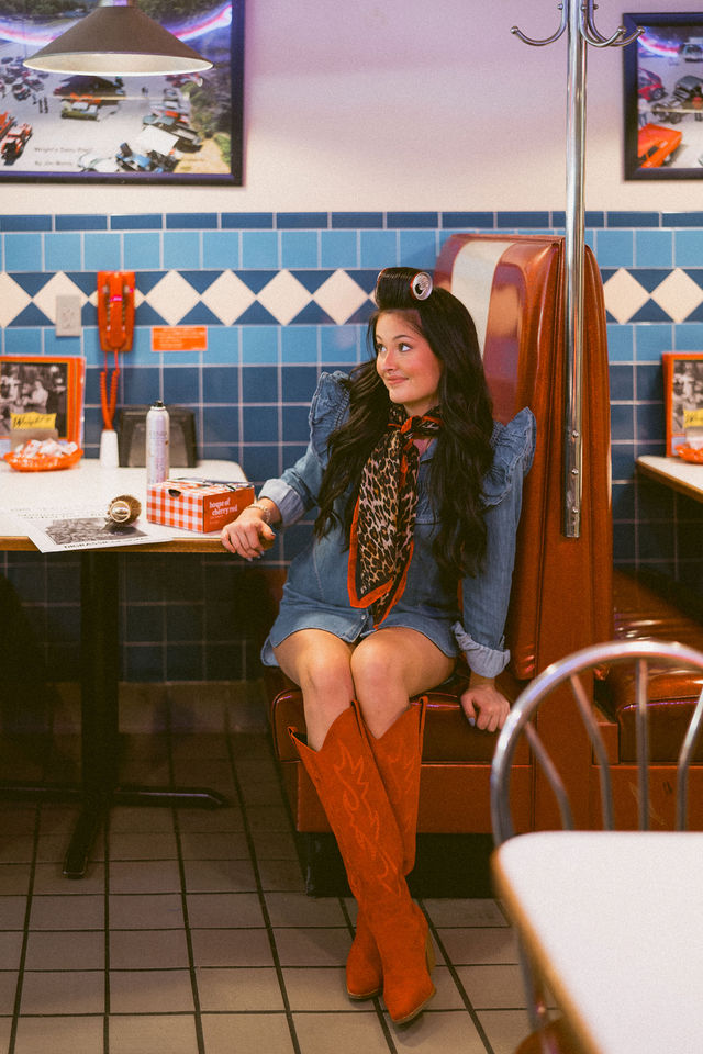 Full-length branding portrait of a hairstylist in a diner booth wearing orange boots.