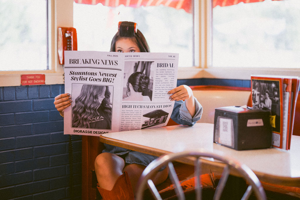Hairstylist holding a DiGrassie Designs newspaper above a diner table.