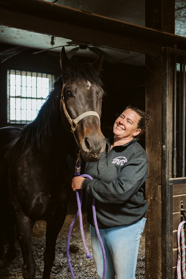 Veterinary professional smiling beside a horse in a stall doorway.